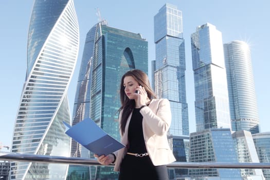 Young beautiful businesswoman with cellphone outdoors at skyscraper background