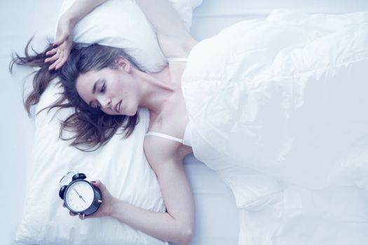 Young beautiful woman waking up with alarm clock