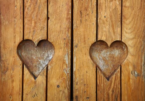 Two heart shaped elements, symbol of love, romance and togetherness, wood carved cut in vintage old grunge natural brown wooden planks texture background, close up