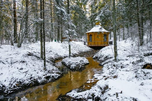 Winter landscape with small river near alcove in a forest