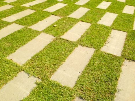A cement walkway that is rectangular and surrounded by green grass.