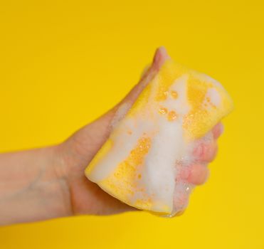 Hand with sponge with foam on yellow background