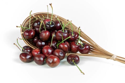 cherries stack in fruit-picker made of a wicker scoop fixed to long handle on white background. 