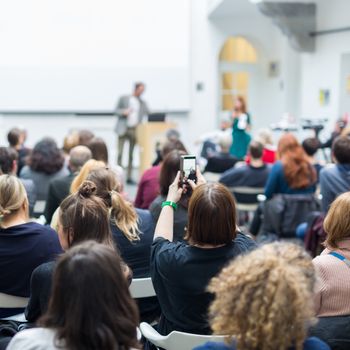 Male speaker giving presentation in lecture hall at university workshop. Audience in conference hall. Rear view of unrecognized participant in audience. Scientific conference event.