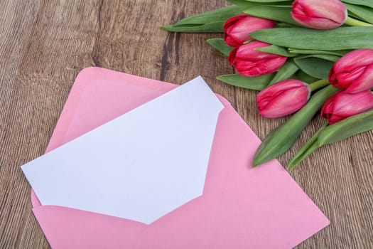 Envelope with sheet of paper and red tulips on a wooden background