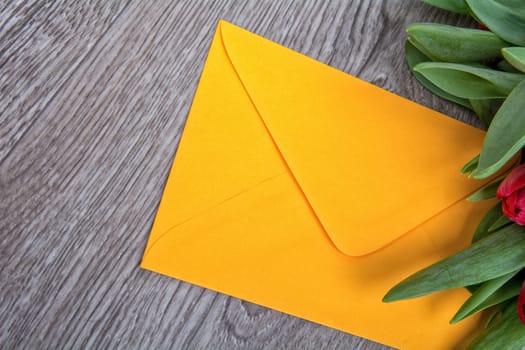 Envelope and red tulip on a wooden background