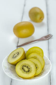 golden kiwi fruit and sliced on dish over white wooden background