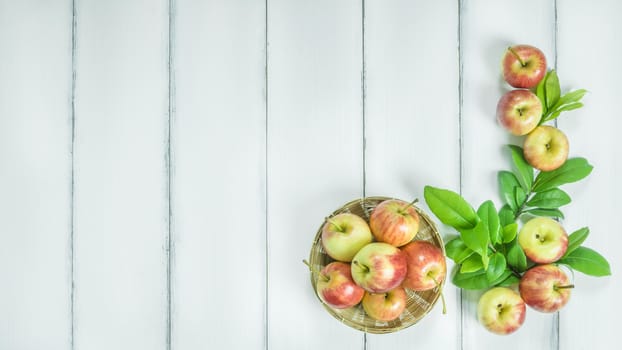 Top view red and yellow apple with leaves and  bamboo basket on  white wooden background with free space for text
