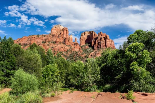 Cathedral Rock, a popular scenic landmark south of Sedona, Arizona with clouds and blue sky and green trees and green bushes.