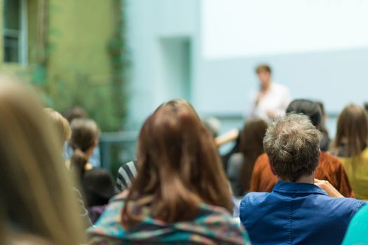 Business and entrepreneurship symposium. Speaker giving a talk at business meeting. Audience in the conference hall. Rear view of unrecognized participant in audience.