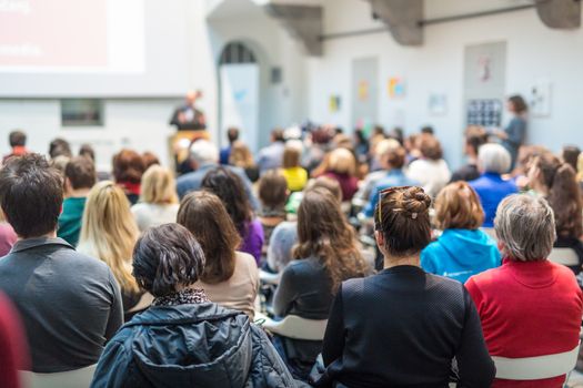 Male speaker giving presentation in lecture hall at university workshop. Audience in conference hall. Rear view of unrecognized participant in audience. Scientific conference event.