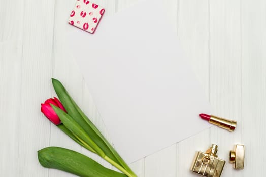 one red tulip, bottle of perfume, lipstick and sheet of paper for your greetings on the background of white wooden board