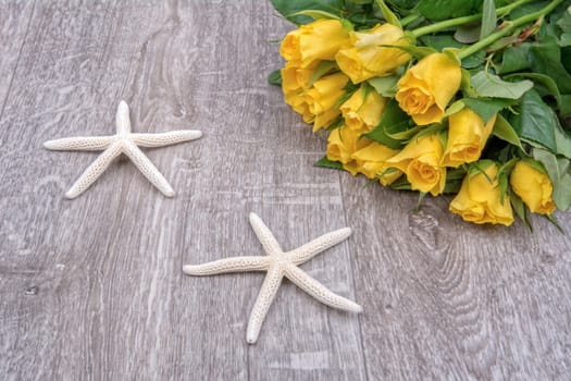 White starfish and yellow roses on a wooden background