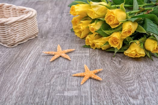 Orange starfishes and yellow roses on a wooden background