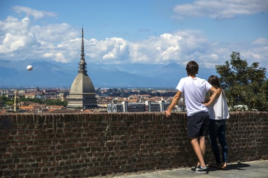 Panoramic view of Turin city center, in Italy, with couple admiring the view in a sunny day, with Mole Antonelliana and Alps in the background