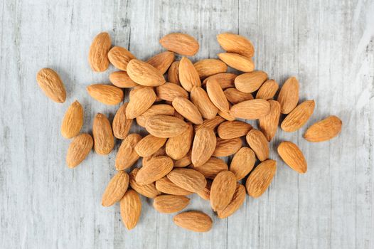 Heap of almonds scattered over white stone board, copy space