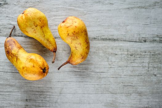 three yellow ripe pears on white wooden background, top view, copy space