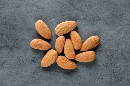 Small heap of almonds scattered over dark stone board, copy space