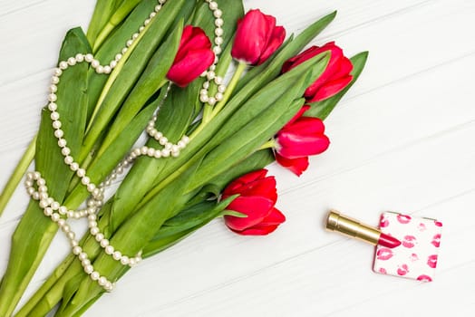 top view beautiful bouquet of red tulips in the necklace, lipstick on the background of white wooden board