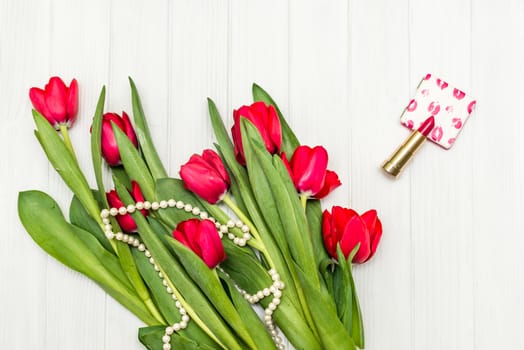 top view beautiful bouquet of red tulips in the necklace, lipstick on the background of white wooden board