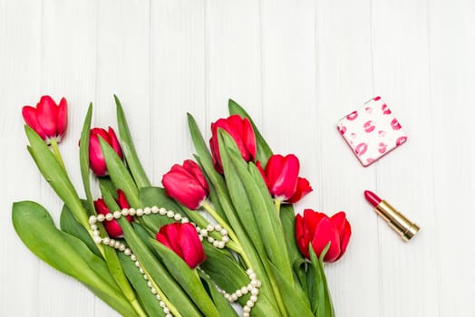 top view beautiful bouquet of red tulips in the necklace, lipstick on the background of white wooden board