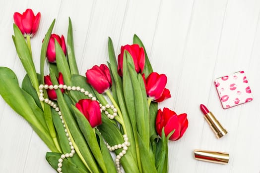 top view beautiful bouquet of red tulips in the necklace, lipstick on the background of white wooden board