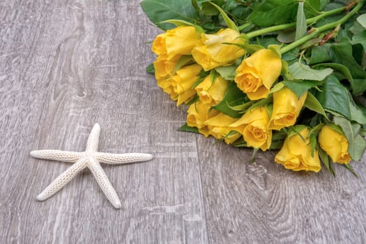 White starfishes and yellow roses on a wooden background
