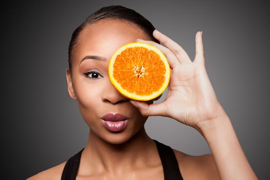 Beautiful healthy happy black asian woman holding delicious orange mandarin fruit in front of eye.