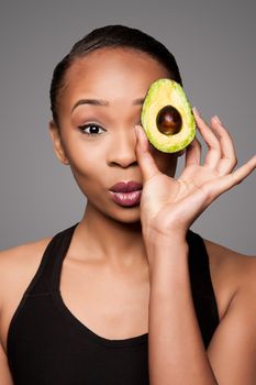 Beautiful healthy happy black asian woman holding delicious avocado super fruit in front of eye.