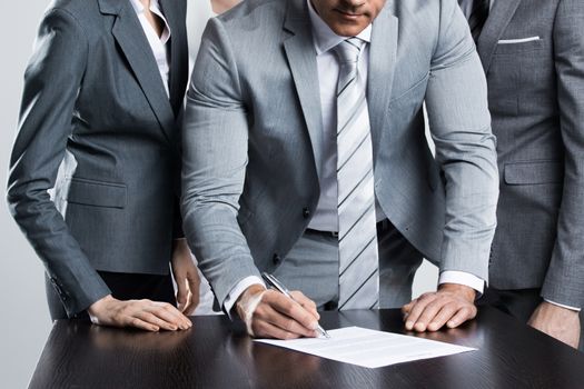 Businessman signing contract while his team is looking at him