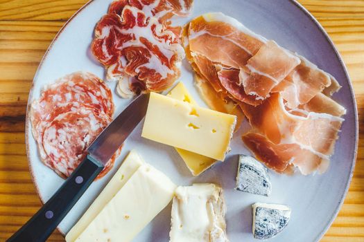 Plate with a variety of Italian cheese and charcuterie, on a wooden table