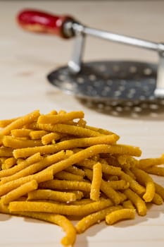 Closeup of Passatelli original Italian pasta over a wooden background and its tool