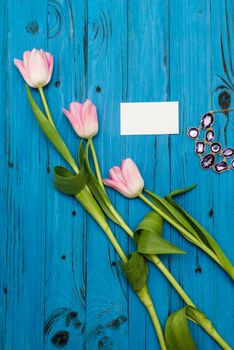 top view beautiful pink tulips, necklace and card of paper for your greetings on the background of blue wooden board