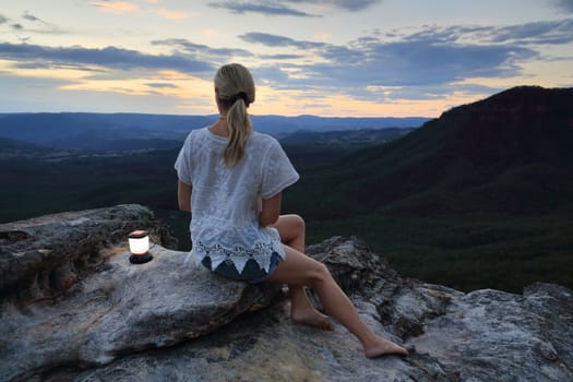 Woman relaxing perched on a rocky outcrop with views high up in the mountains to the valley below and beyond.

Location:  narrowneck, Blue Mountains, Australia,