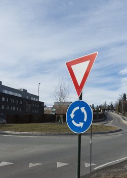 a round about in Norway with a building, some trees and a few cars