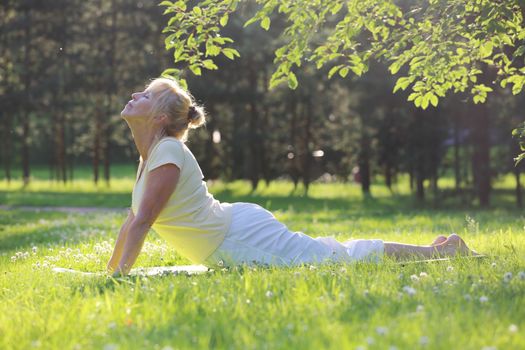 Beautiful mature woman practice yoga in summer park