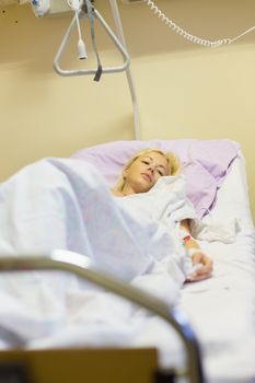 Bedridden female patient lying in hospital bed, recovering after surgery.
