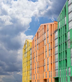 Fragment of a multicolored facade of the modern multi-story apartment complex against the background of the sky with storm clouds
