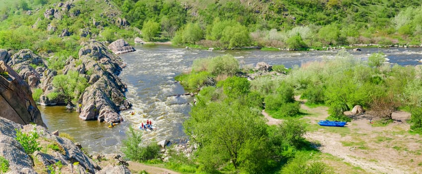 Panorama of the river section with rapids and rock outcrops and trees on its banks on a spring day
