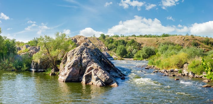 Panorama of the river section with rapids and rock outcrops and trees on its banks on a summer day
