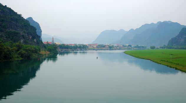 Amazing natural landscape at Quang Binh, Viet Nam on day, boat moving on river,  riverside house with mountains behind, green field beside water, beautiful scene for Vietnam travel