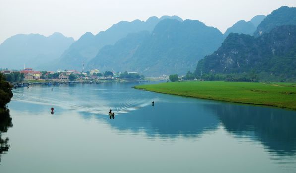 Amazing natural landscape at Quang Binh, Viet Nam on day, boat moving on river,  riverside house with mountains behind, green field beside water, beautiful scene for Vietnam travel