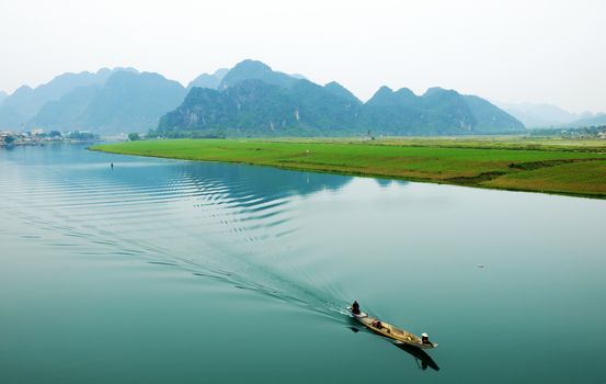 Amazing natural landscape at Quang Binh, Viet Nam on day, boat moving on river,  riverside house with mountains behind, green field beside water, beautiful scene for Vietnam travel