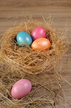 Decorations for Easter.   Colored chicken eggs in a nest of hay on a wooden background
