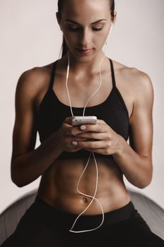 Shot of a beautiful young woman setting the music playlist for the workout.