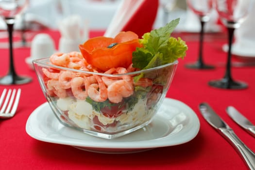 Seafood salad with shrimps and fresh vegetables, on a serving table. On a red tablecloth close-up