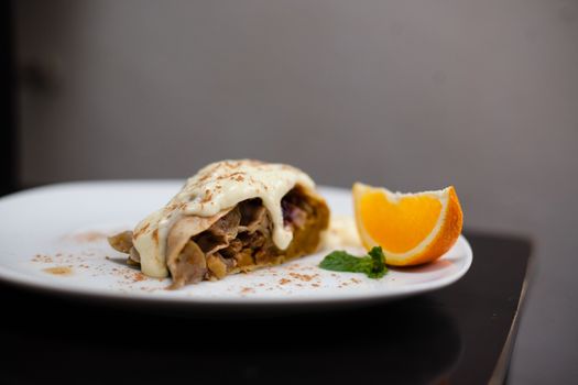 A piece of apetite strudel with orange, nut, cinnamon pod on a white plate