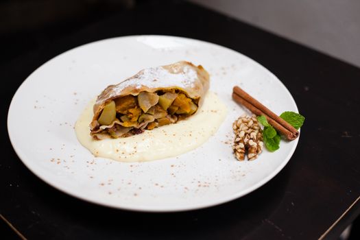 A piece of apetite strudel with orange, nut, cinnamon pod on a white plate