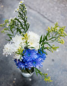 A simple bouquet of flowers in a vase on the pavement close up