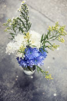 A simple bouquet of flowers in a vase on the pavement close up